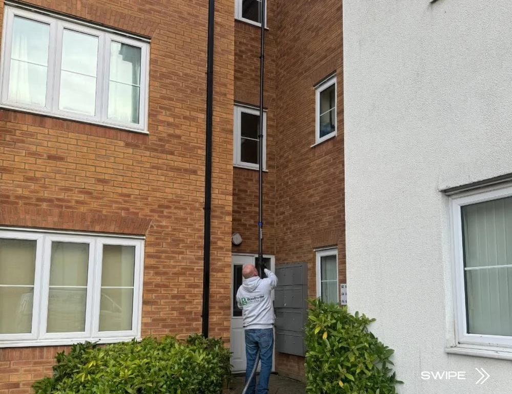 Gutter cleaning pole between brick buildings by Boothville Services.