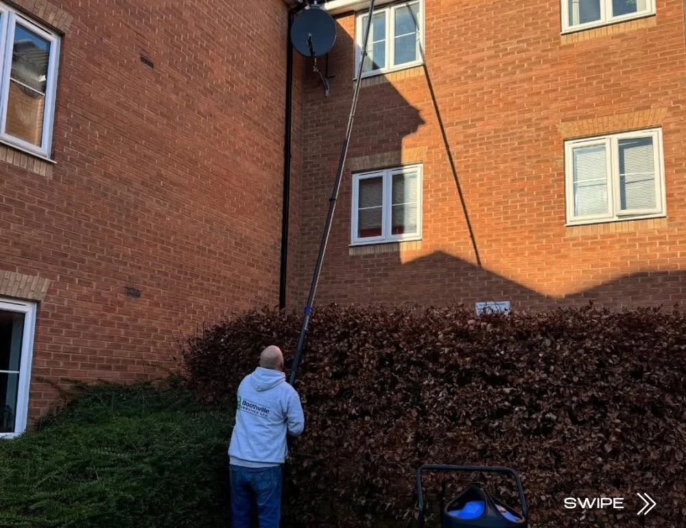 Worker clearing gutters with a high-reach pole by Boothville Services.