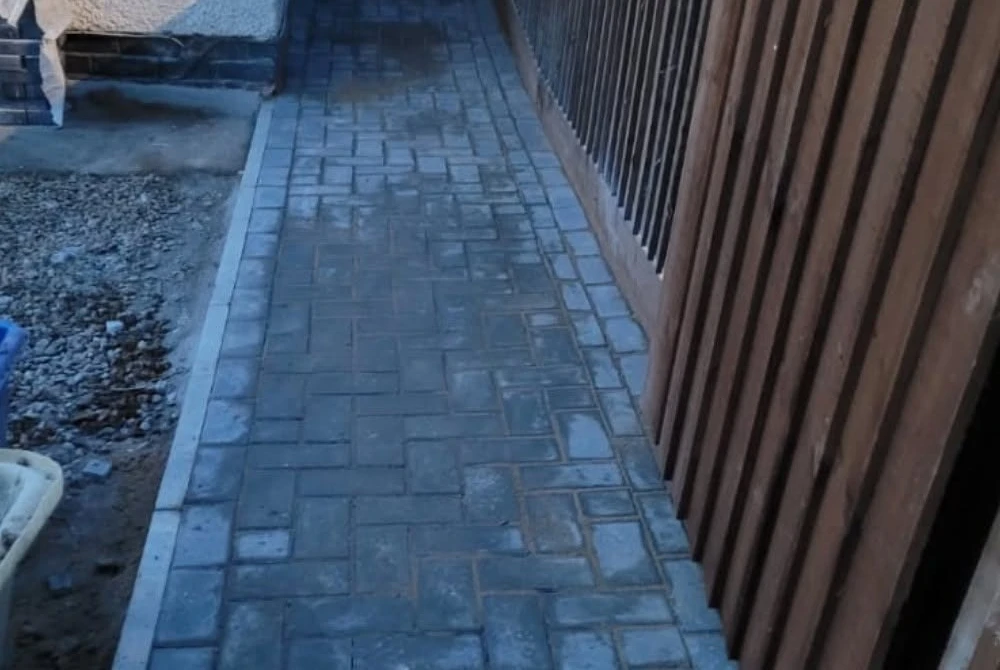 Narrow block-paved side path beside a timber fence by Boothville Services.