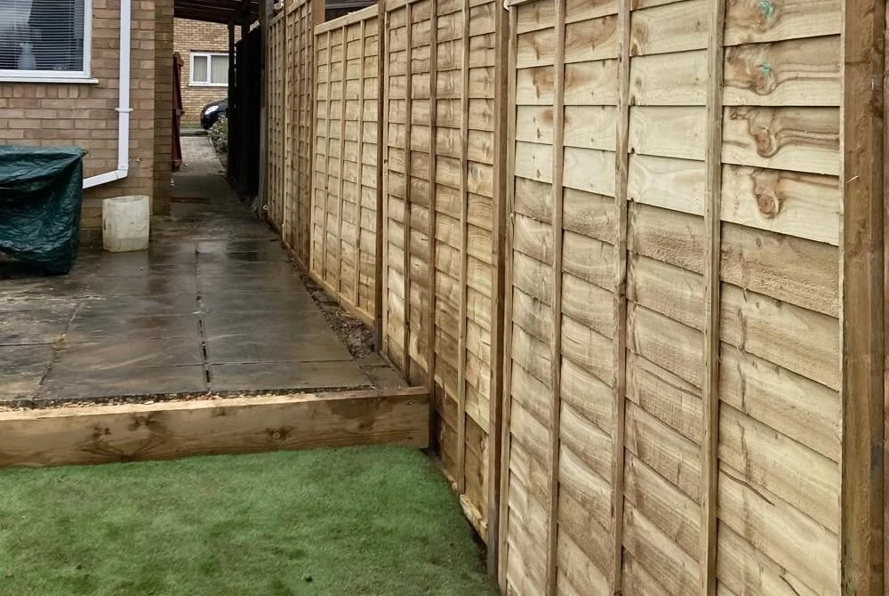 Pale timber fence beside a paved passage by Boothville Services.